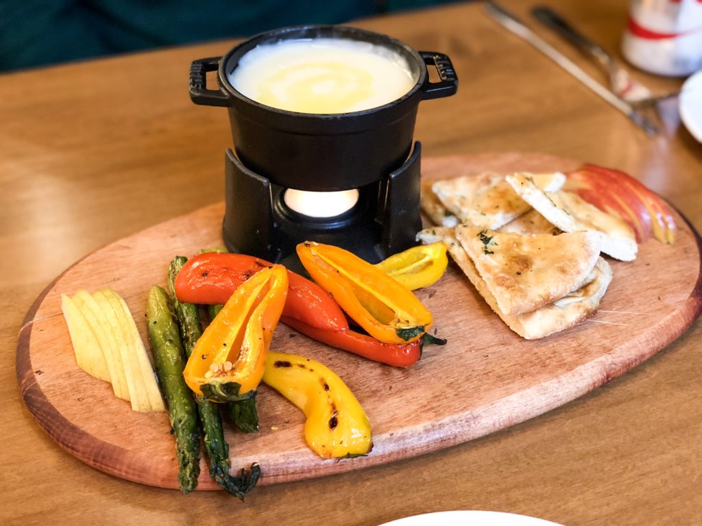 A plate of vegetables and bread with a black fondue pot sitting on a wooden tray