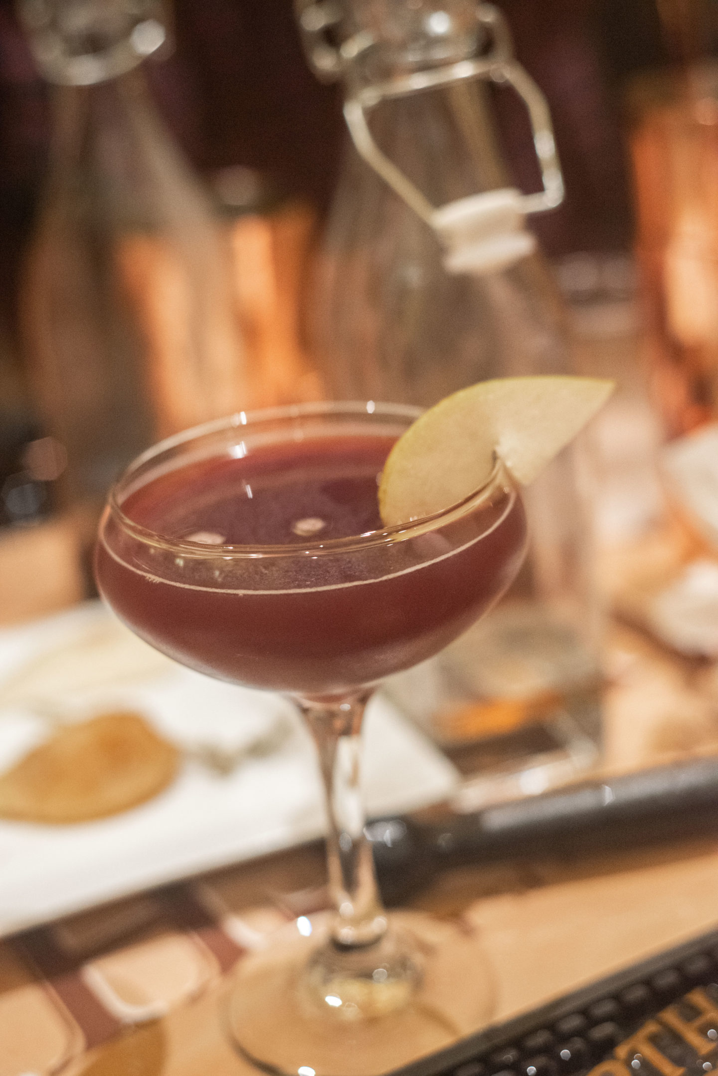A dark colored cocktail garnished with a pear