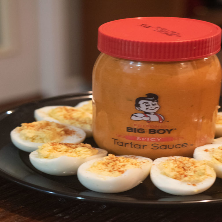 Deviled Eggs sitting on a black plate with a jar of Frisch's Spicy Tartar Sauce