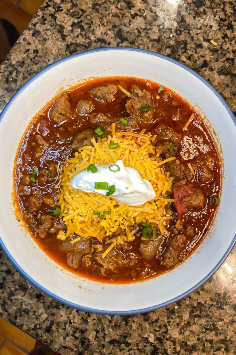 chili in a bowl with sour cream, cheese, and scallions
