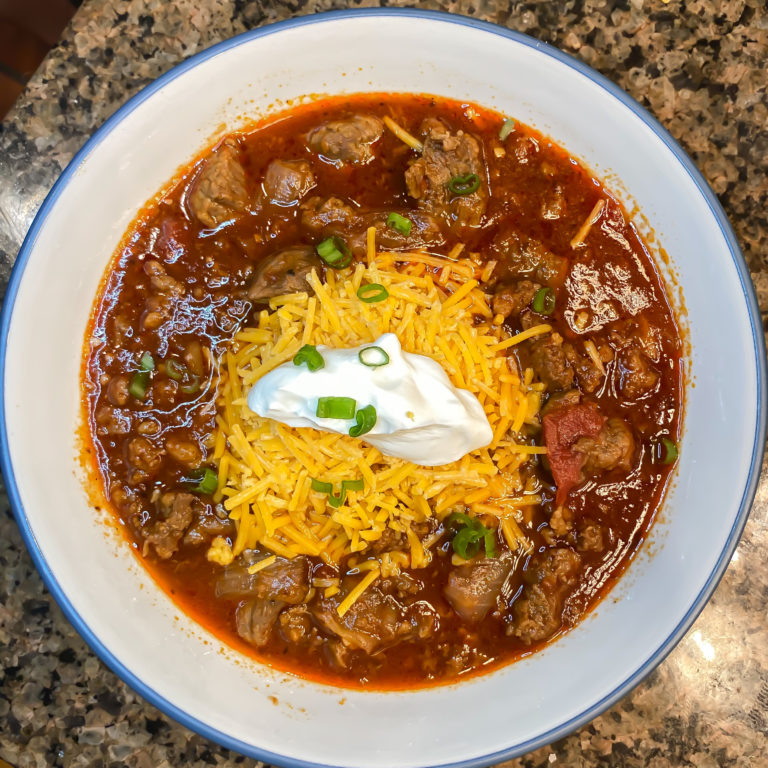 chili in a bowl with sour cream, cheese, and scallions