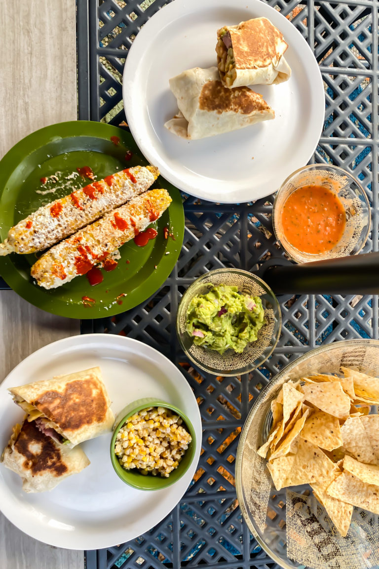 california burritos, elote, guacamole, and salsa on a patio table